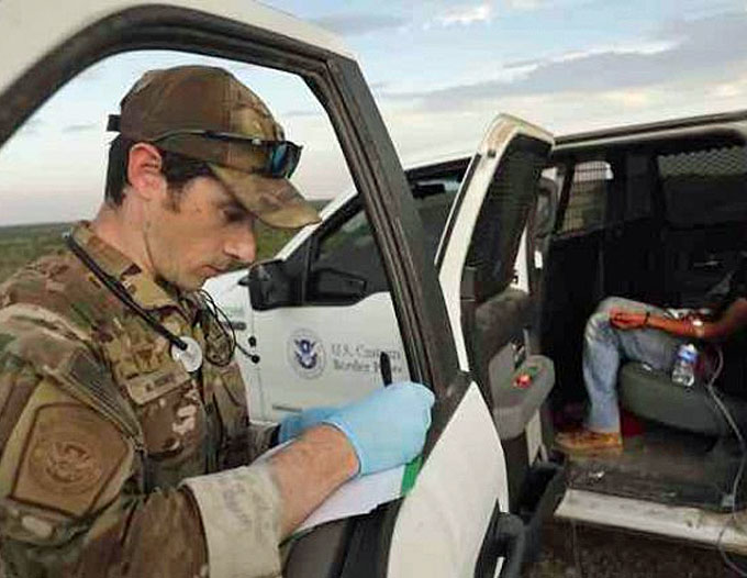 A U.S. Border Patrol Search, Trauma, and Rescue (BORSTAR) agent creates a medical report while an IV is administered to a migrant found suffering from dehydration and exhaustion. (Courtesy of CBP by Glenn Fawcett)