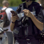 Female,Police,Officer,Standing,Next,To,Motorbike,,Checking,Mobile,Phone